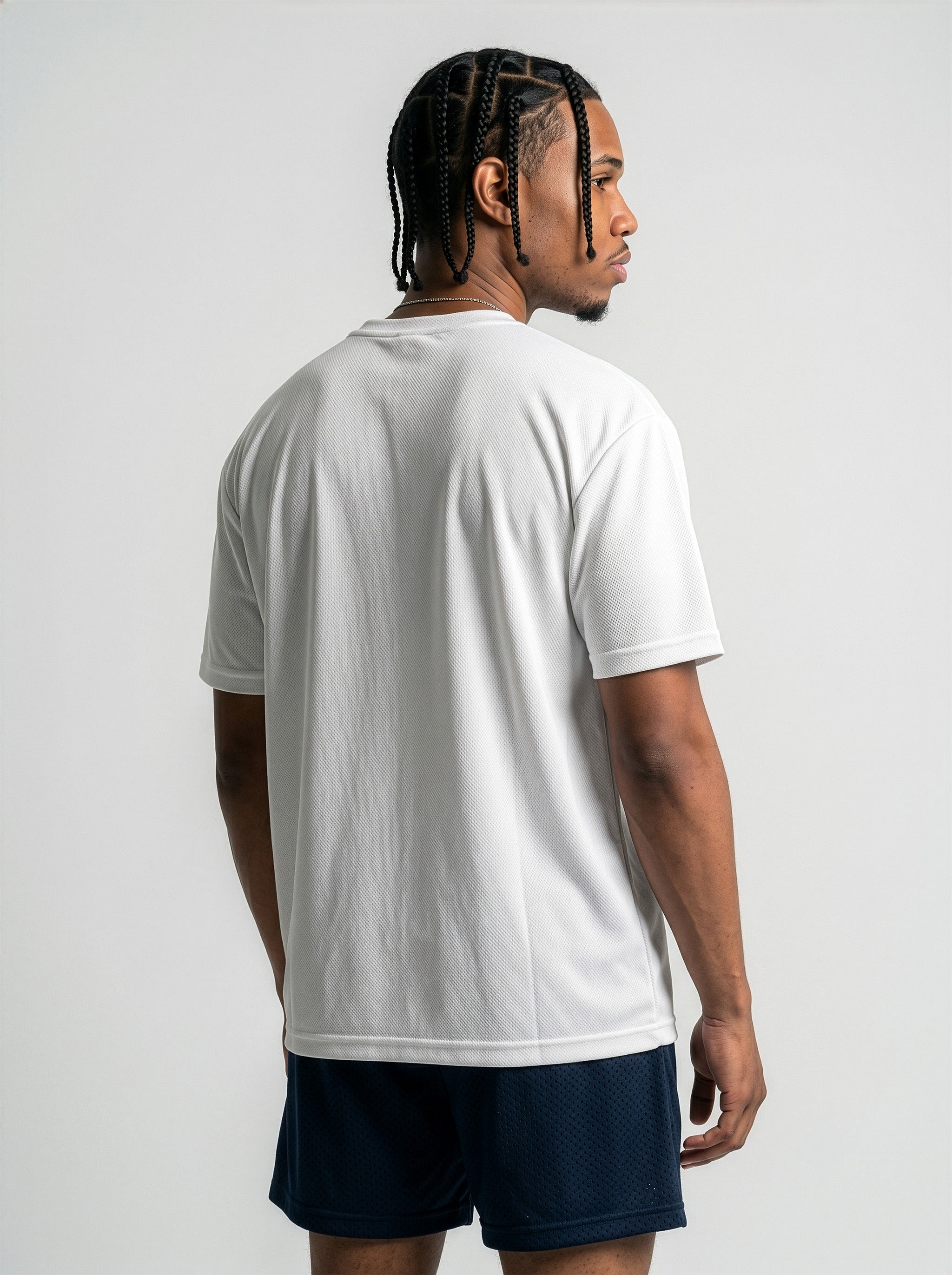 Back View Commercial studio catalog photography of model Jason featuring sharp box braids, wearing the AfroRock Core Performance T-Shirt in White. Low-angle front-facing view highlighting the minimalist crewneck collar detailing, structured shoulders, and athletic drape of the performance fabric. Clean high-key medium-gray studio background.