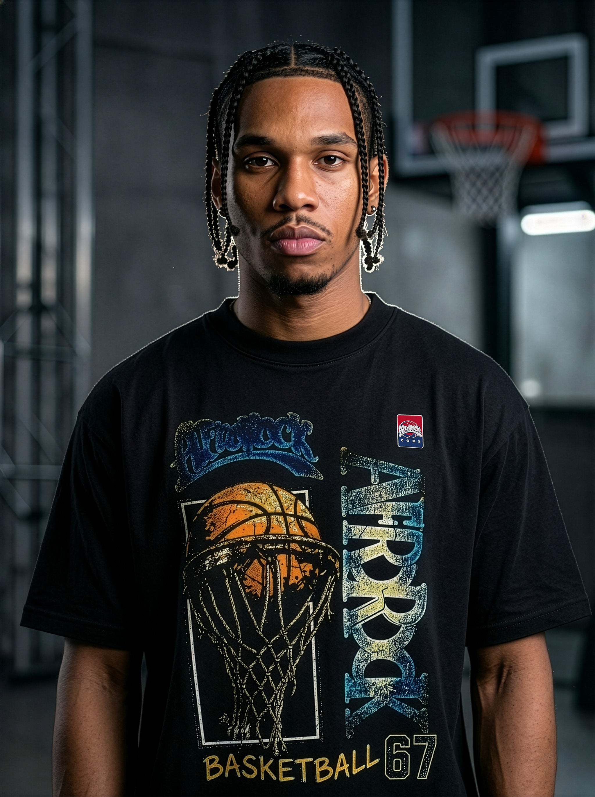 Studio product photography of model Jason in the AfroRock Core streetwear collection. He wears the AfroRock Basketball Vintage Graphic Tee in Pitch Black, an oversized 260gsm cotton shirt with an expansive front graphic of a basketball and hoop, a vintage weather-crackle print finish, and an athletic team badge. Industrial studio lighting highlights a premium sport-heritage lifestyle aesthetic.