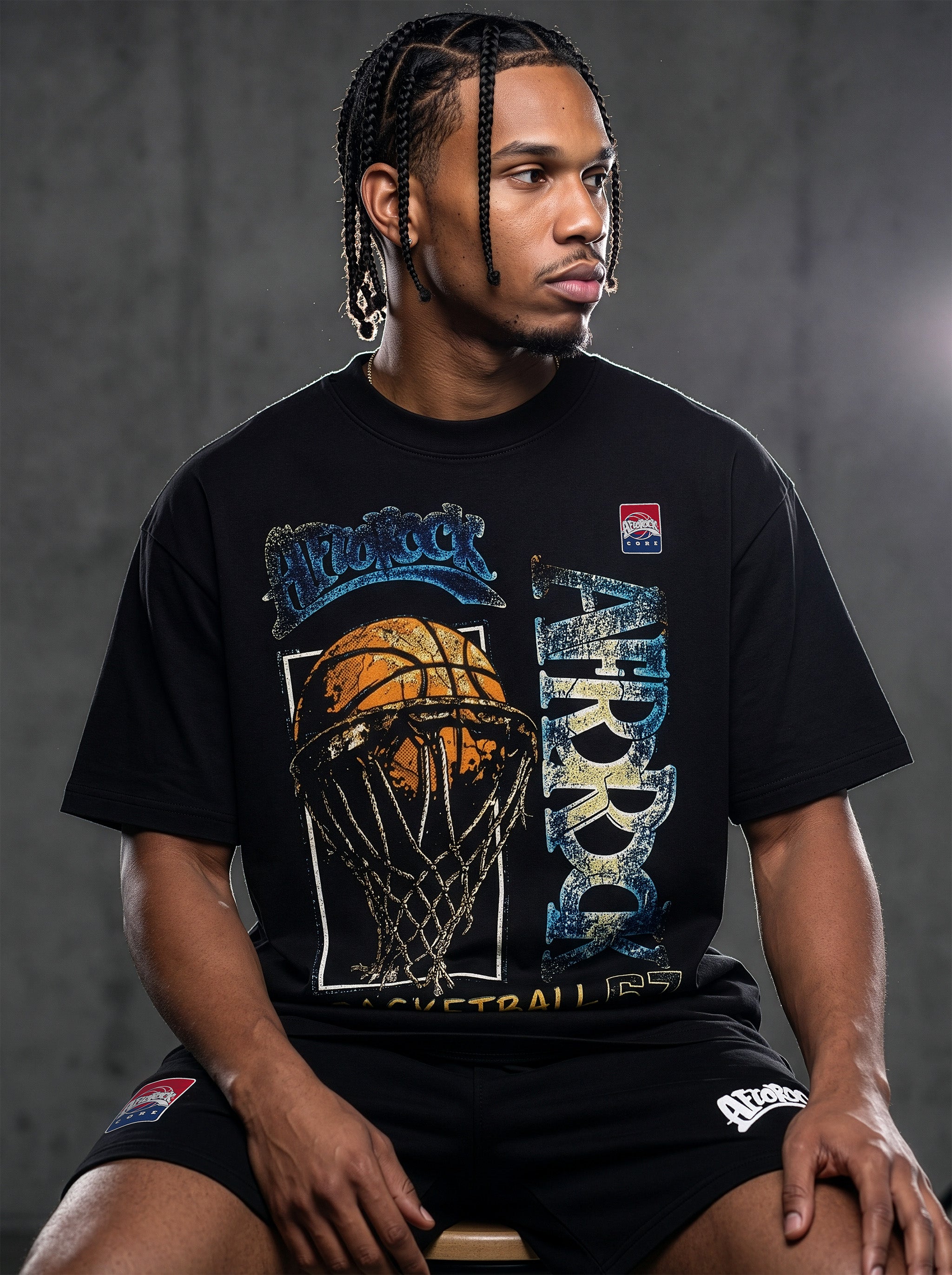 Studio product photography of model Jason in the AfroRock Core streetwear collection. He wears the AfroRock Basketball Vintage Graphic Tee in Pitch Black, an oversized 260gsm cotton shirt with an expansive front graphic of a basketball and hoop, a vintage weather-crackle print finish, and an athletic team badge. Industrial studio lighting highlights a premium sport-heritage lifestyle aesthetic.