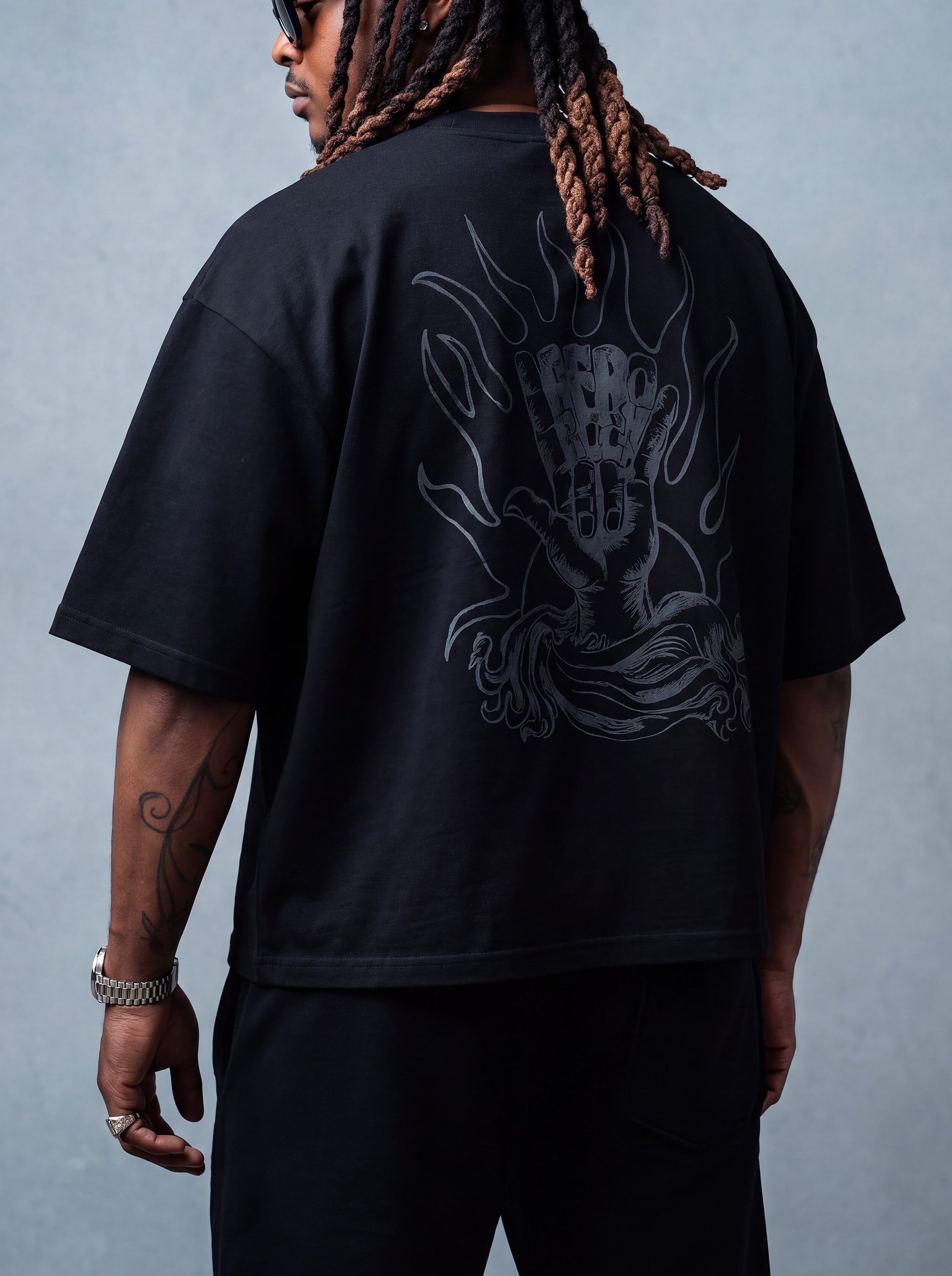 Brand founder Kal Afrorock modeling the Elite AfroRock Culture Oversized Boxy T-Shirt in Pitch Black. Heavyweight 300gsm seamless cotton streetwear tee featuring custom hand-drawn graphics and an intentional drop-shoulder silhouette.