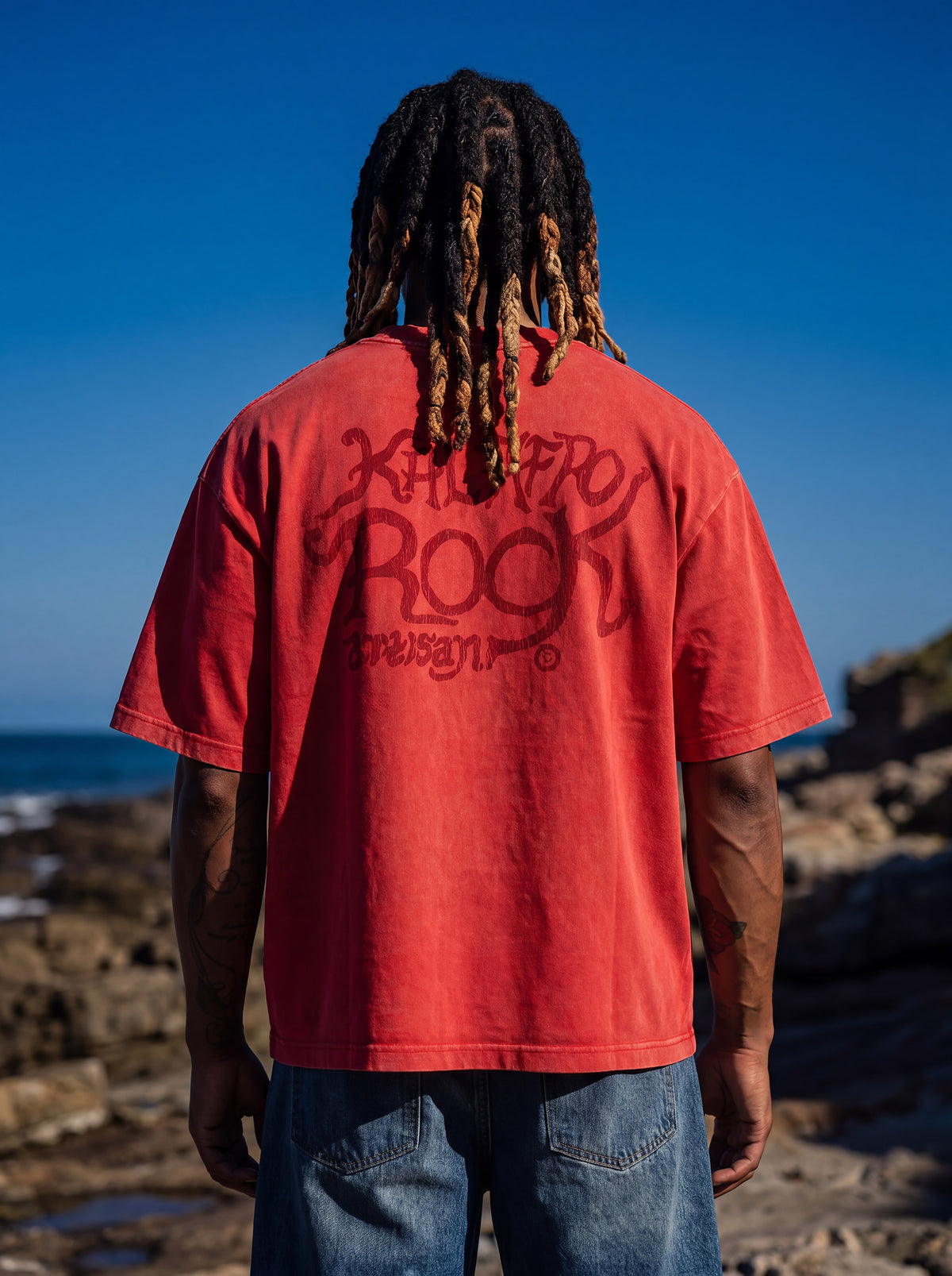Brand founder Kal Afrorock modeling the AfroRock Ishiagu Vintage Mineral Wash Boxy Tee in Fade Crimson. Premium 360gsm heavyweight cotton streetwear t-shirt featuring a custom hand-drawn West African Ishiagu Lion graphic.