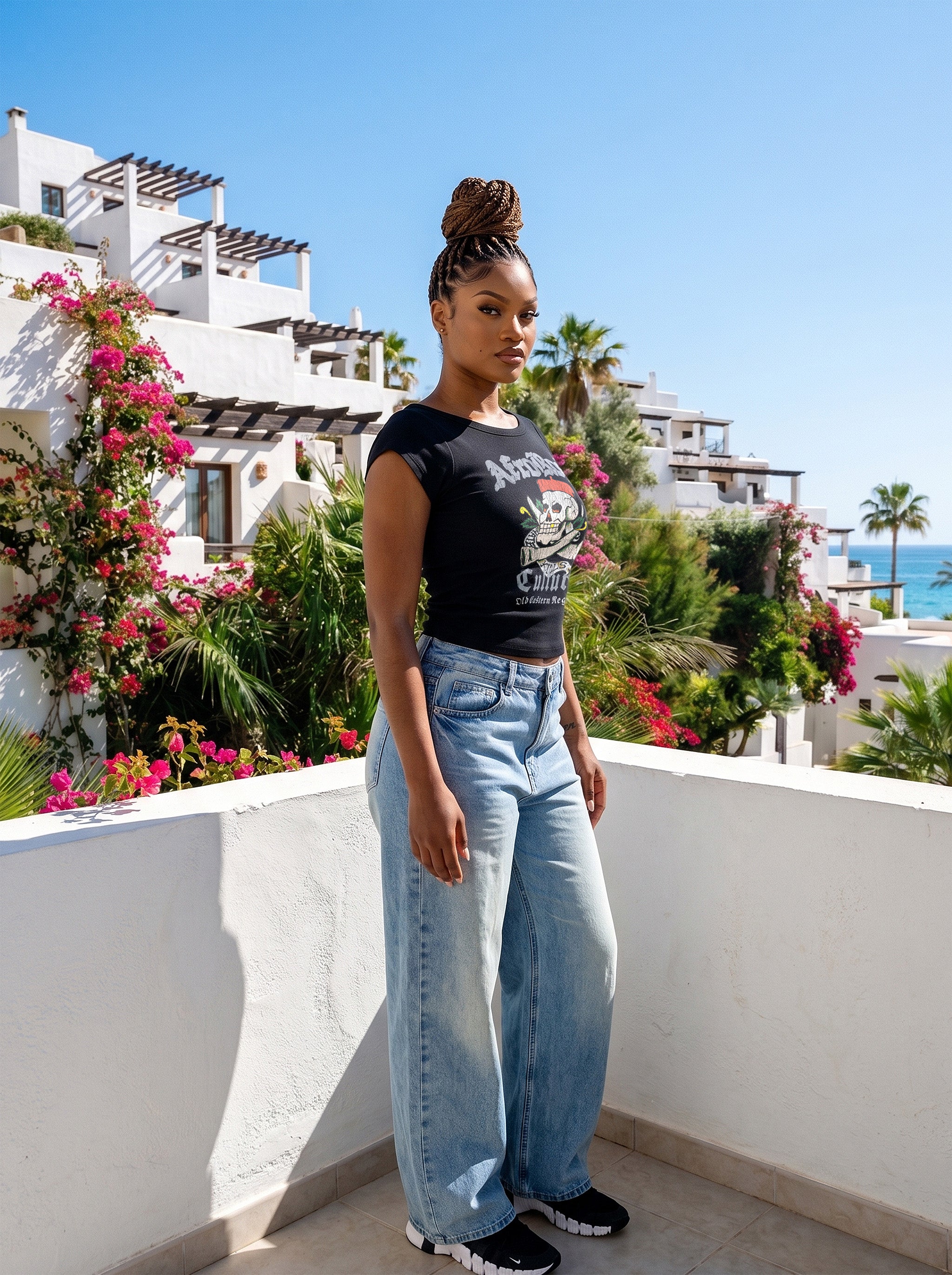 Model Nina in the AfroRock Chief Skull Horns Wide Neck Baby Tee in Pitch Black. Fine-ribbed bodycon graphic tee featuring an original hand-drawn 1883 West African heritage skull design and artisan back branding by AfroRock.