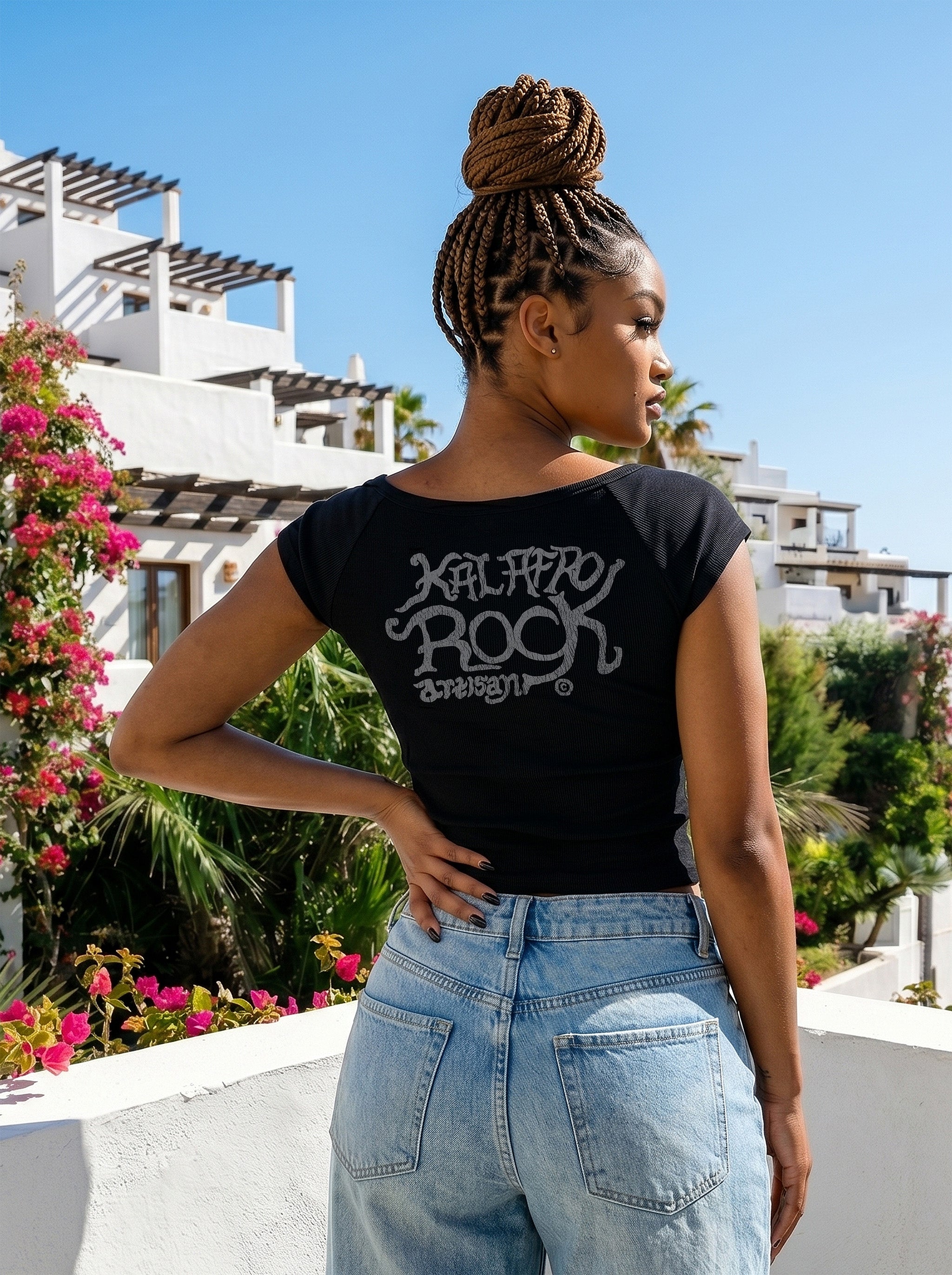 Rear View of Model Nina in the AfroRock Chief Skull Horns Wide Neck Baby Tee in Pitch Black. Fine-ribbed bodycon graphic tee featuring an original hand-drawn 1883 West African heritage skull design and artisan back branding by AfroRock.