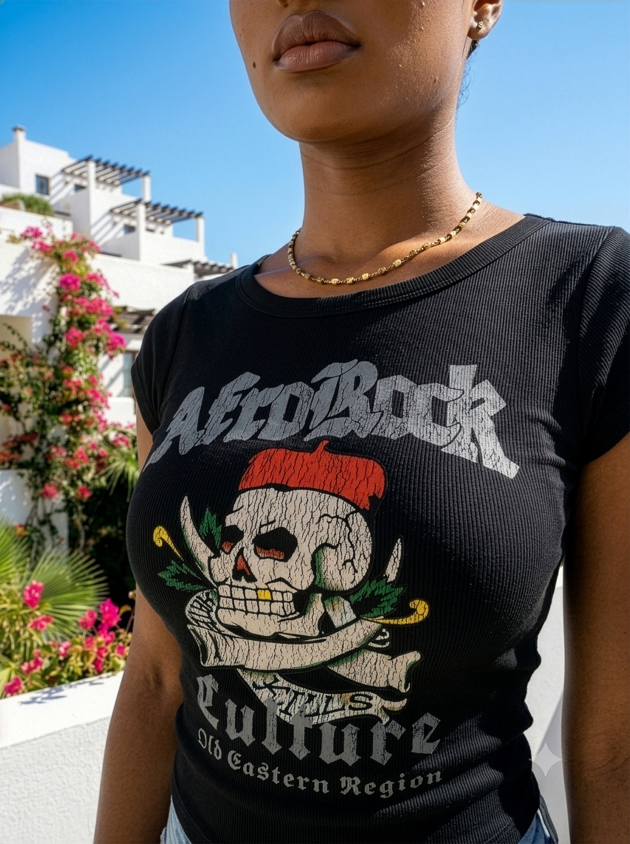 Model Nina in the AfroRock Chief Skull Horns Wide Neck Baby Tee in Pitch Black. Fine-ribbed bodycon graphic tee featuring an original hand-drawn 1883 West African heritage skull design and artisan back branding by AfroRock.